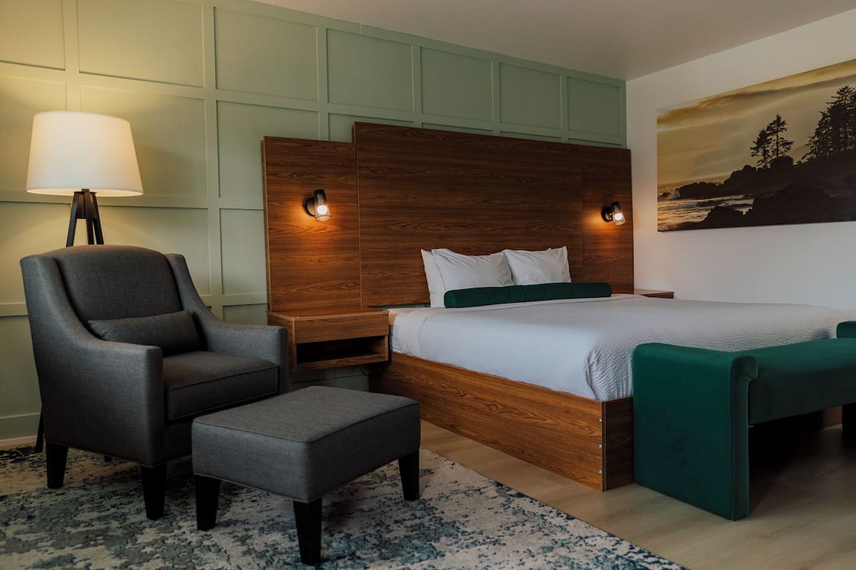 Ein modernes Schlafzimmer mit einem Holzkopfteil, einem grauen Sessel, einem passenden Hocker und einer grünen Bank.