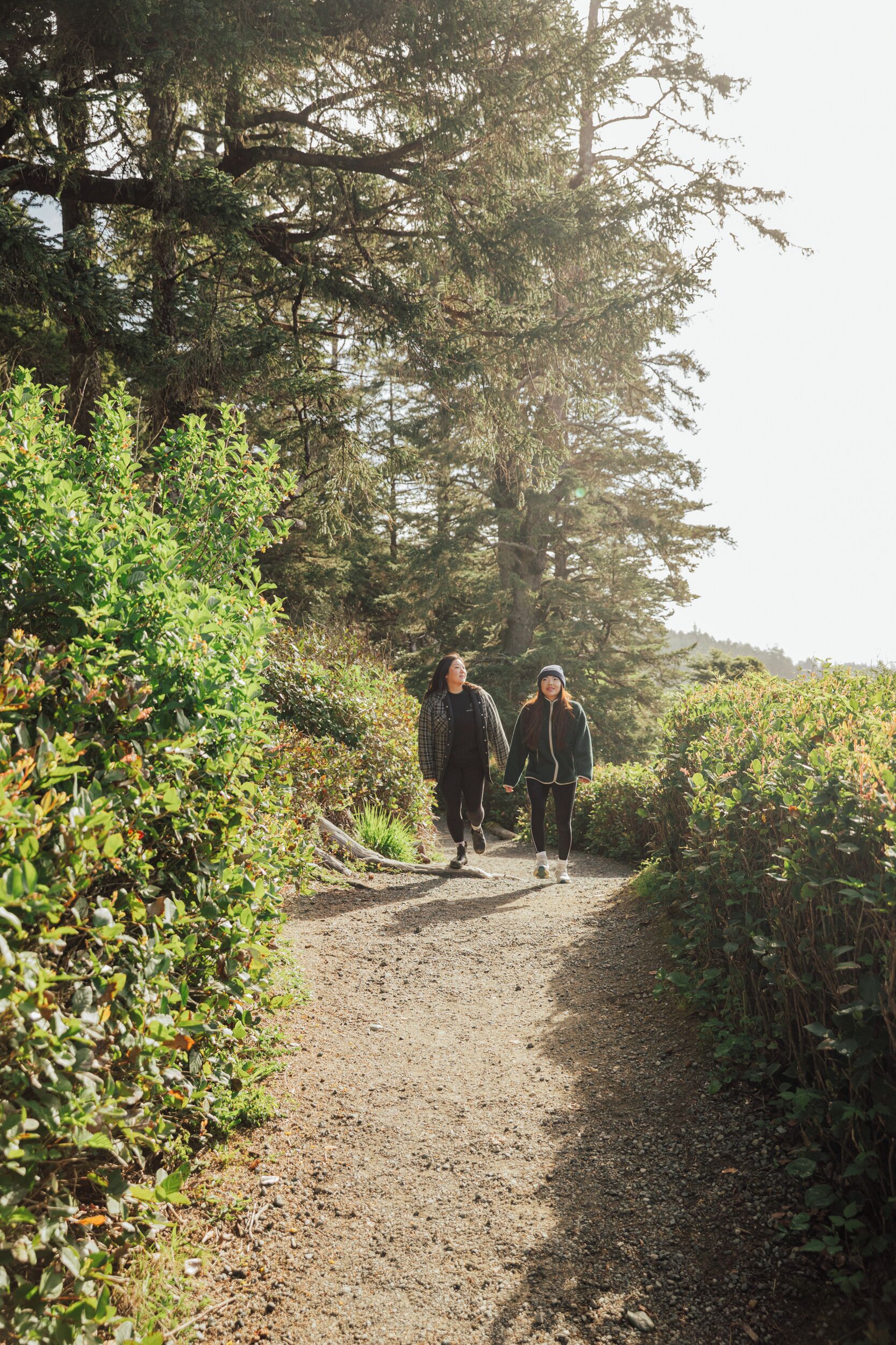 Two people walking on a gravel path surrounded by greenery.