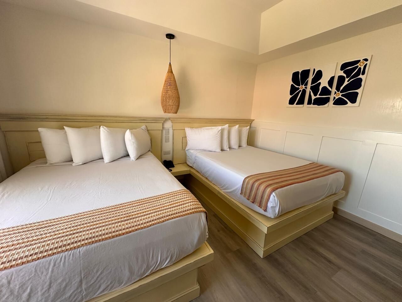 A hotel room with two beds, a hanging light fixture, and wall art.