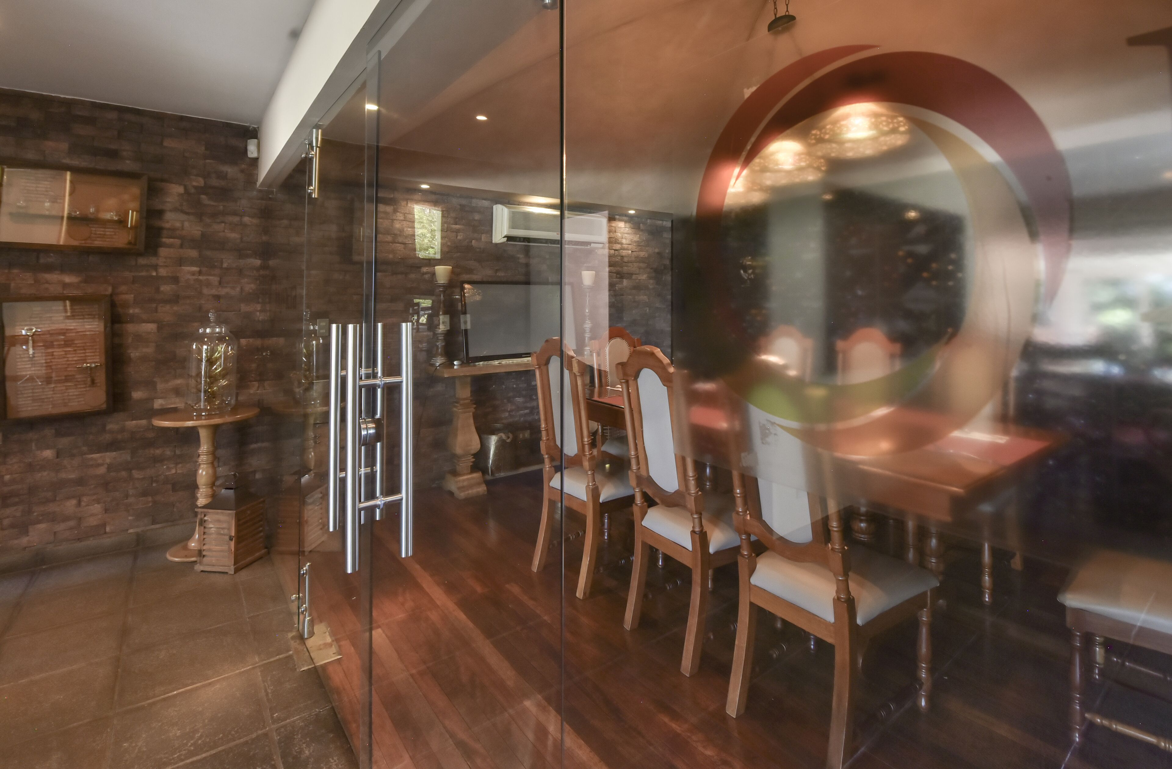 A dining area with wooden chairs, a glass partition, and a brick wall.
