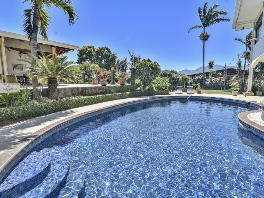 A swimming pool with a tiled edge, surrounded by palm trees and a building with a sign.