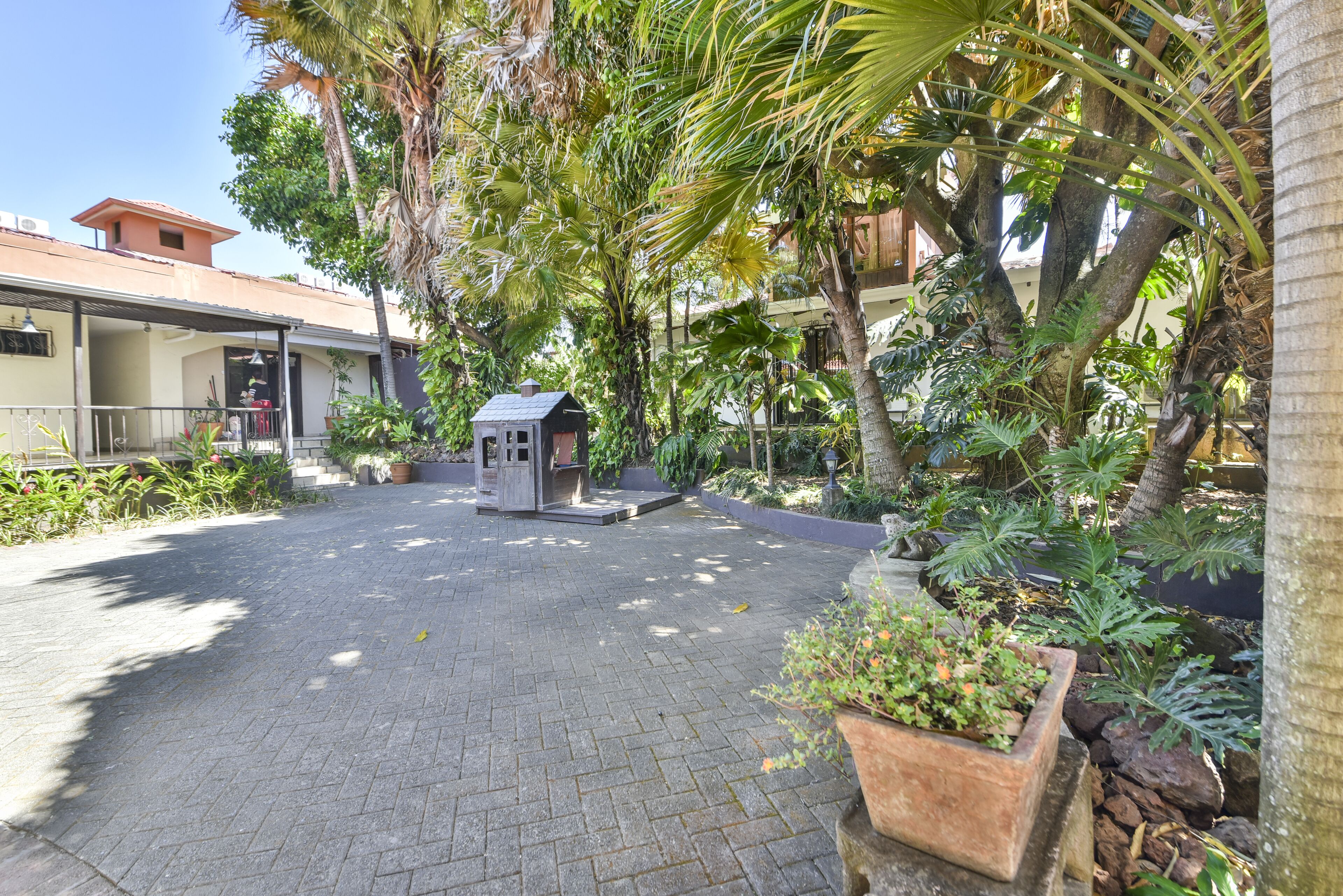 A courtyard with a small gazebo, paved walkway, and lush greenery.