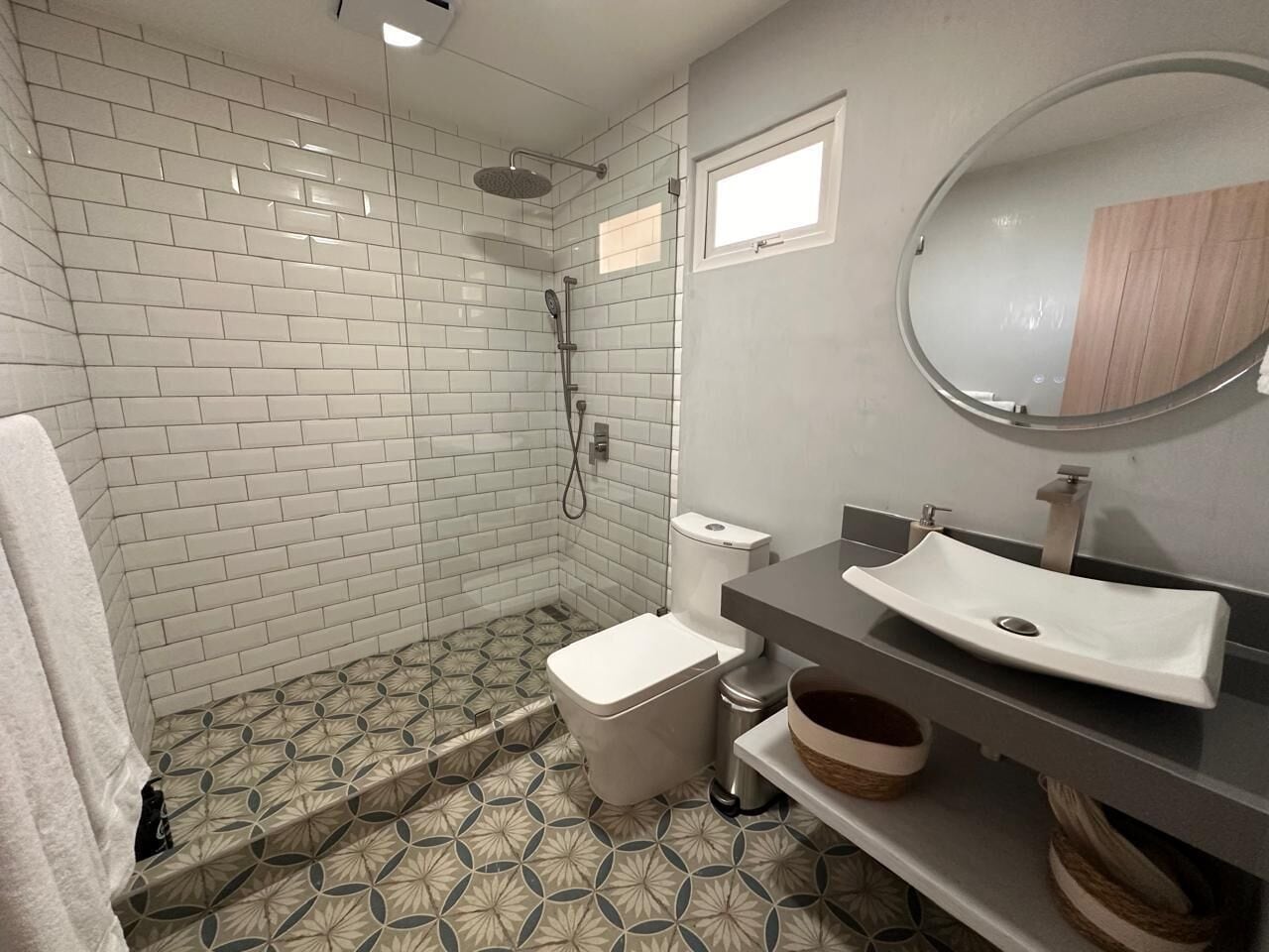 A bathroom with white subway tiles, a shower, a toilet, a sink, and a mirror.
