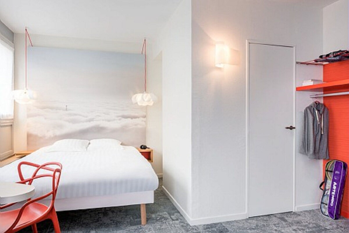 Een slaapkamer met een bed, een stoel, een nachtkastje, een wandplank en een deur.