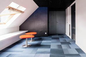 Un pasillo con techo inclinado, un mural de estrellas en la pared, dos sillones naranja y un suelo estampado.