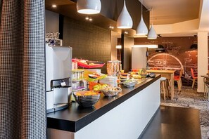 Una cocina moderna con mesas tipo bufé, que incluye un refrigerador, máquina de café y diferentes alimentos.