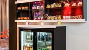 Un mini-bar avec des en-cas et des boissons, un réfrigérateur rempli de boissons et une chaise.