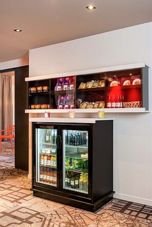 Un minibar con aperitivos y bebidas, un refrigerador con bebidas, y una silla.
