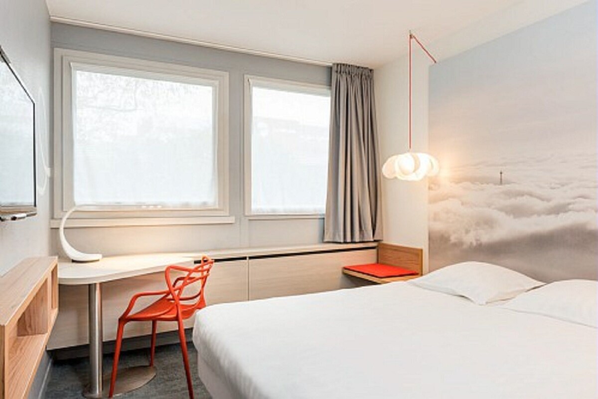 Een hotelkamer met een bed, een bureau, een stoel, een raam met gordijnen en een wanddecoratie.