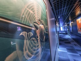Interior moderno de un tren con diseño curvo, una pantalla digital y un suelo estampado.