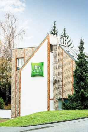 Een modern gebouw met een groen bord waarop 'ibis Styles Hotel' staat.