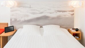 Un lit avec vue sur les nuages, une table de chevet avec une tablette et une petite table de nuit avec des écouteurs.