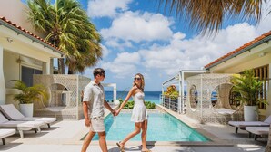 A couple walking by a pool with lounge chairs and palm trees.