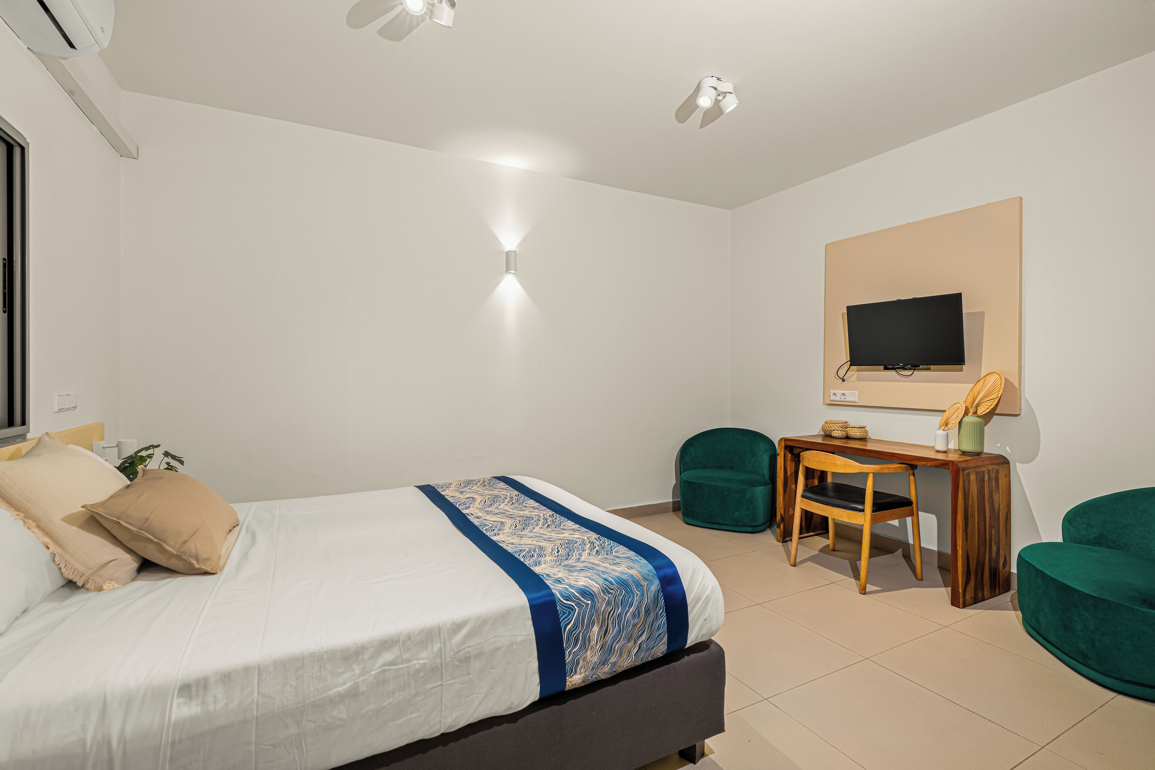 A bedroom with a bed, a desk, a chair, a television, and a green armchair.