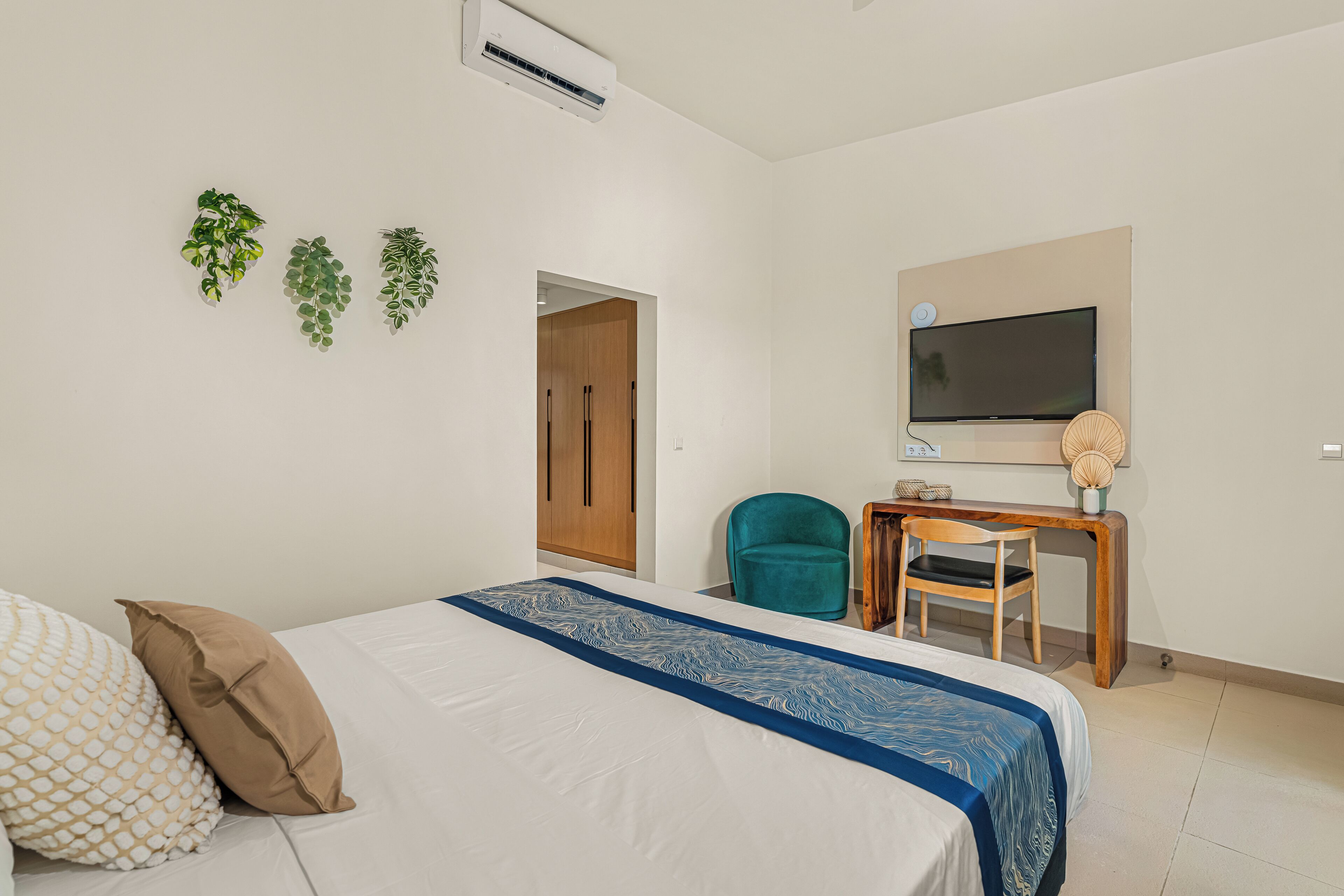 A bedroom with a bed, a desk, a chair, a TV, and a door.