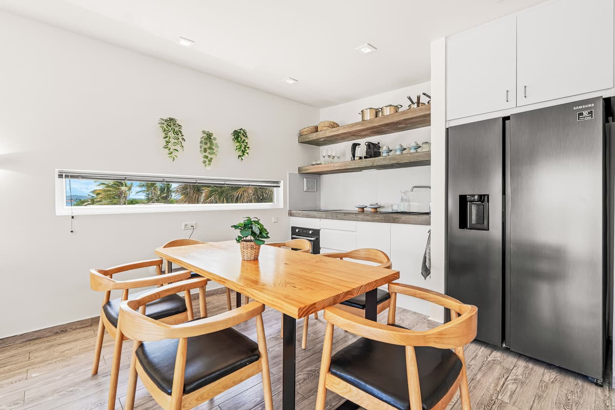A modern kitchen with a stainless steel refrigerator, wooden cabinets, and a dining area with a wooden table and chairs.