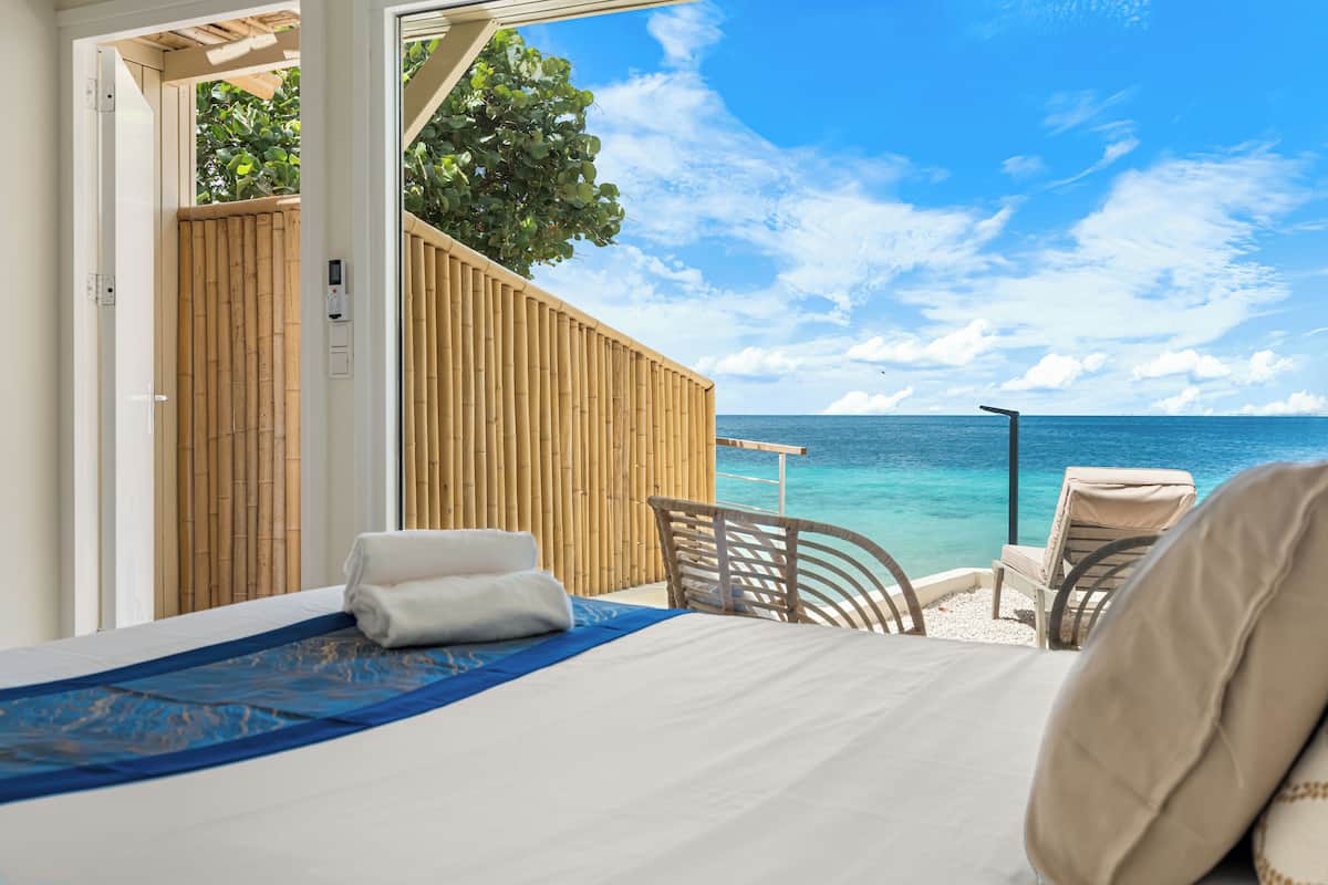 A bedroom with a bed, a chair, and a view of the ocean.