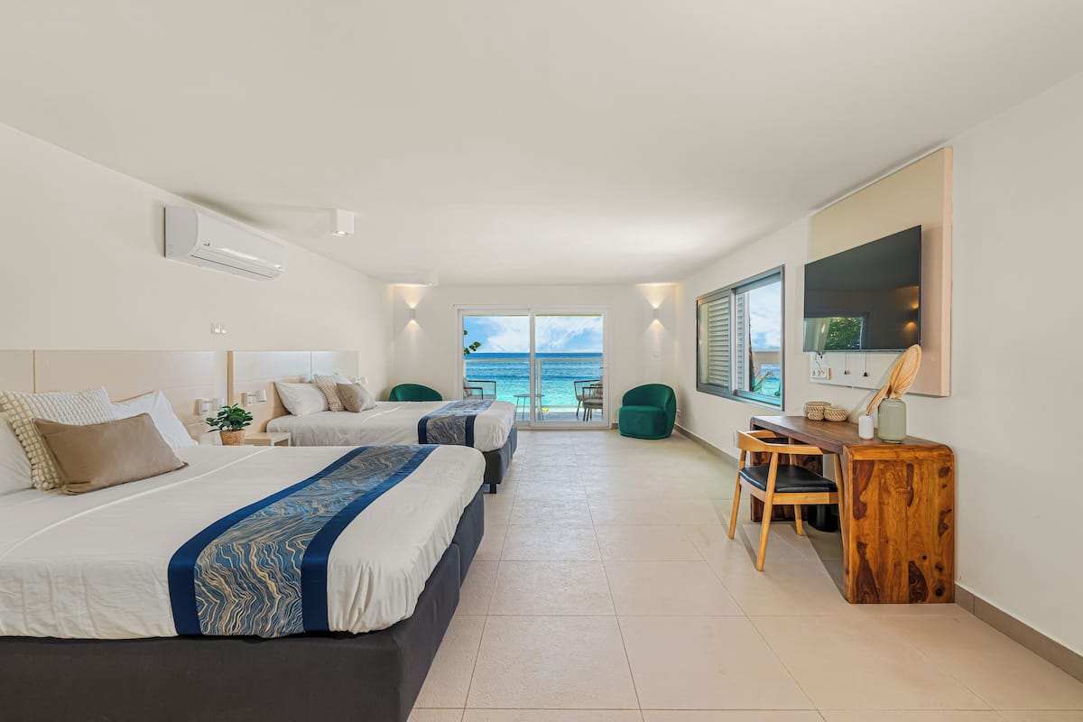 A modern hotel room with two beds, a desk, and a view of the ocean.