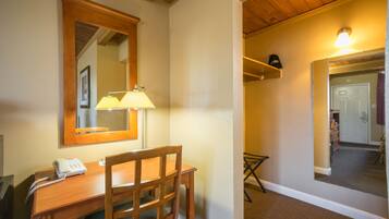A hotel room with a wooden desk, a telephone, a mirror, and a lamp.