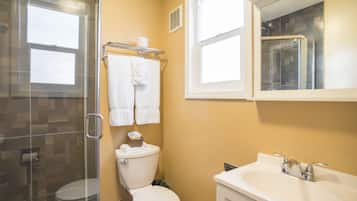 Ein Badezimmer mit Duschkabine aus Glas, Toilette, Waschbecken und Fenster.