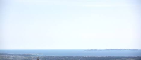 A panoramic view of a coastal landscape with a distant shoreline, trees, and a clear sky.