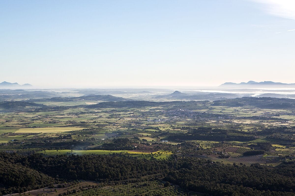 An aerial view of a rural landscape with rolling hills, fields, and scattered buildings.