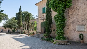 A courtyard with stone paving, a building with green shutters, and a plaque on the wall.