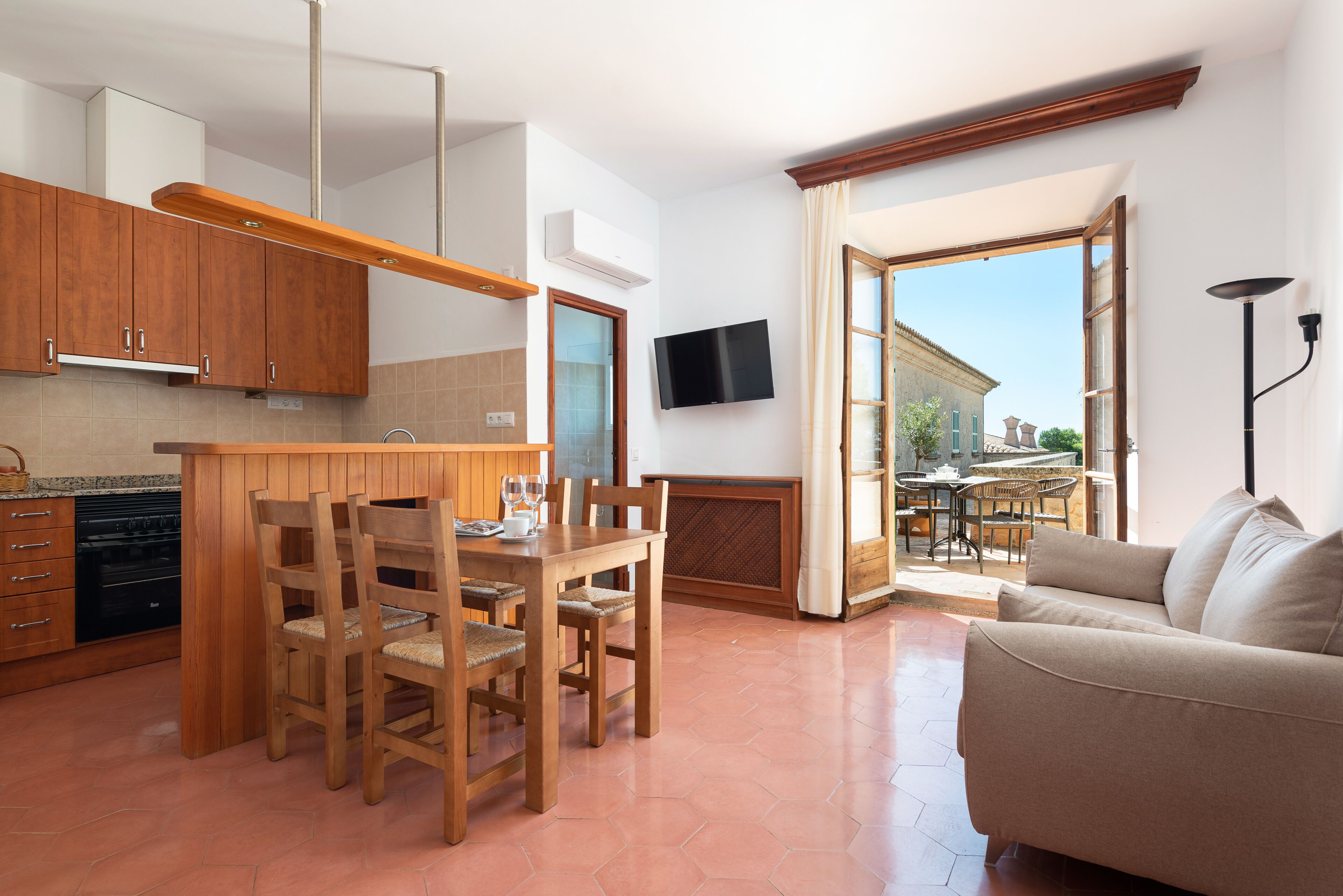 Een moderne keuken met houten kasten, een zithoek met stoelen, een bank en een aan de muur bevestigde televisie.