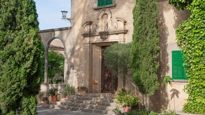 A historic building with a stone facade, green shutters, and a central entrance with steps leading up to it.