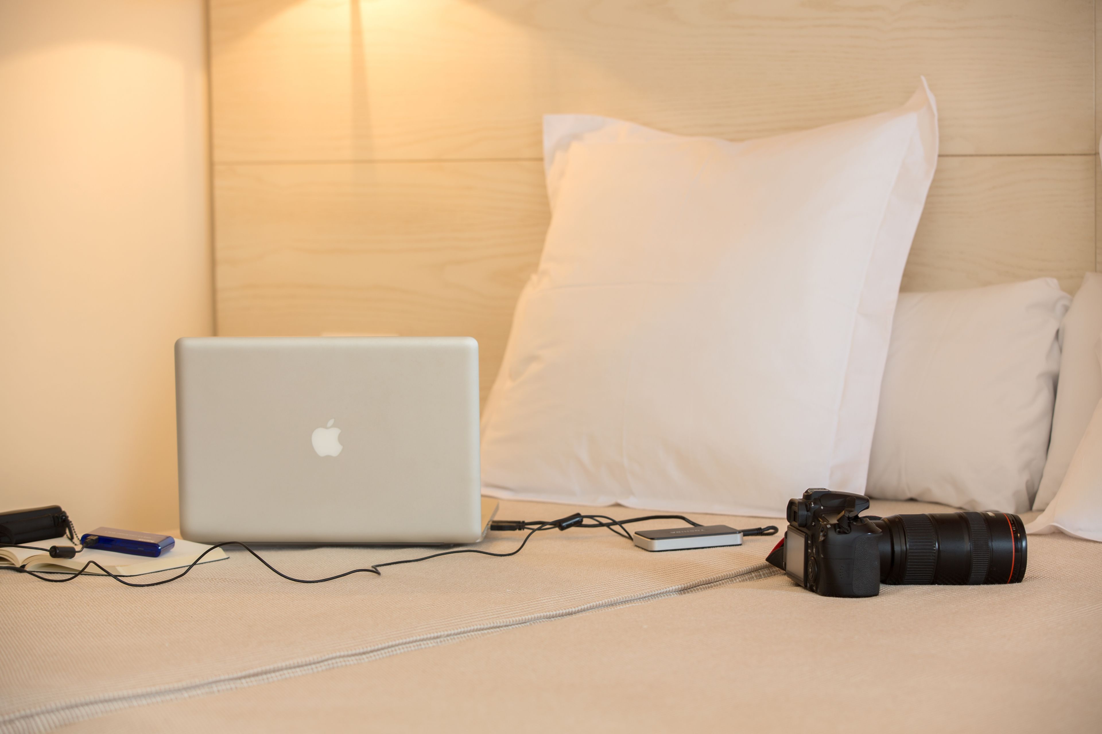 A bed with a laptop, camera, and charger on a textured bedspread.