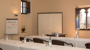 Un salón de conferencias con mesas dispuestas para una reunión, una pizarra con mensaje de bienvenida en varios idiomas y vistas a un edificio histórico a través de una ventana.