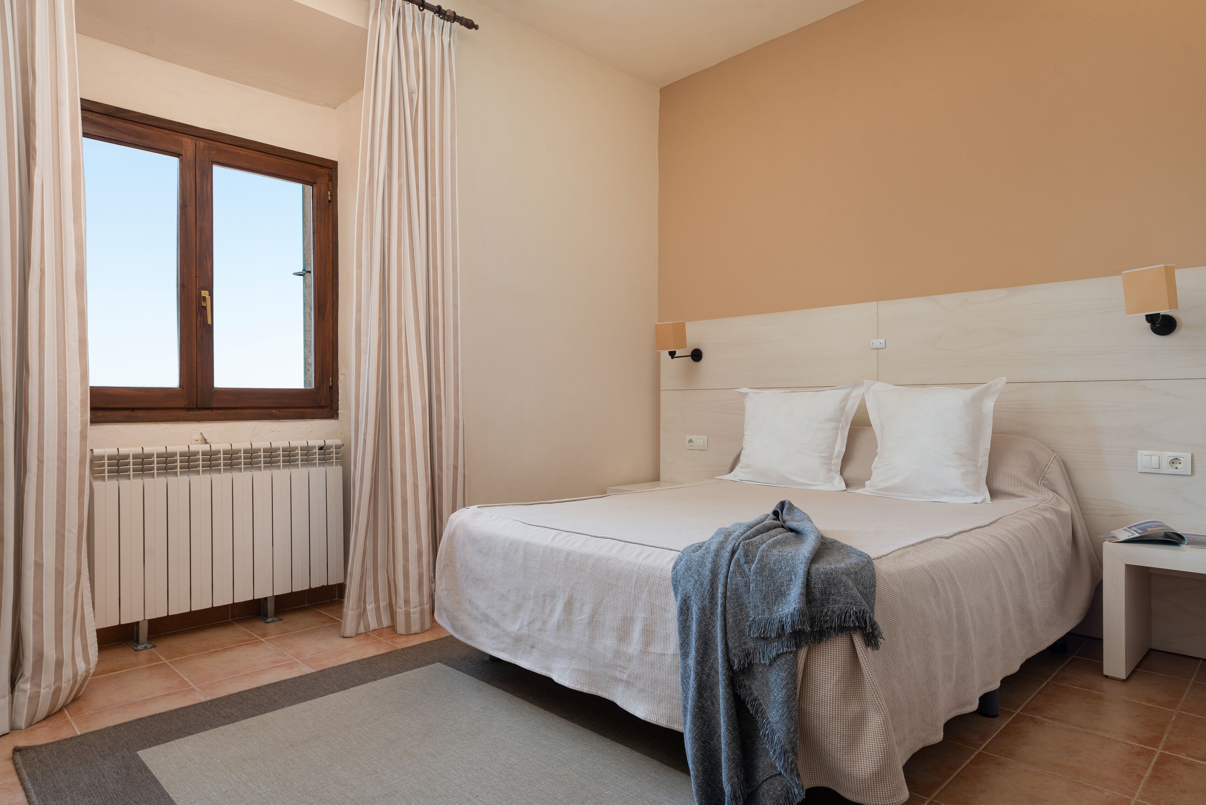 Ein Schlafzimmer mit einem Bett, einem Nachttisch, einem Fenster mit Vorhängen und einer Heizung.