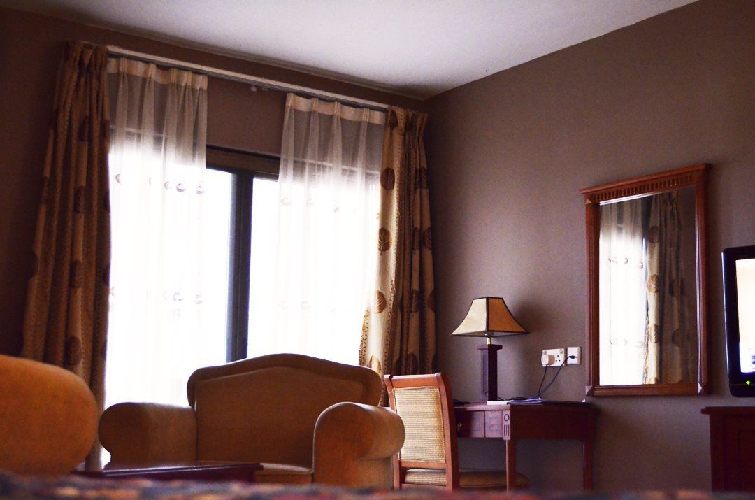 A hotel room with a large window, a chair, a small table with a lamp, and a television.