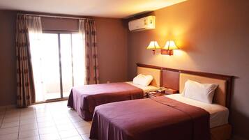 Habitación de hotel con dos camas, una puerta corrediza de vidrio, un aire acondicionado y una lámpara fijada a la pared.