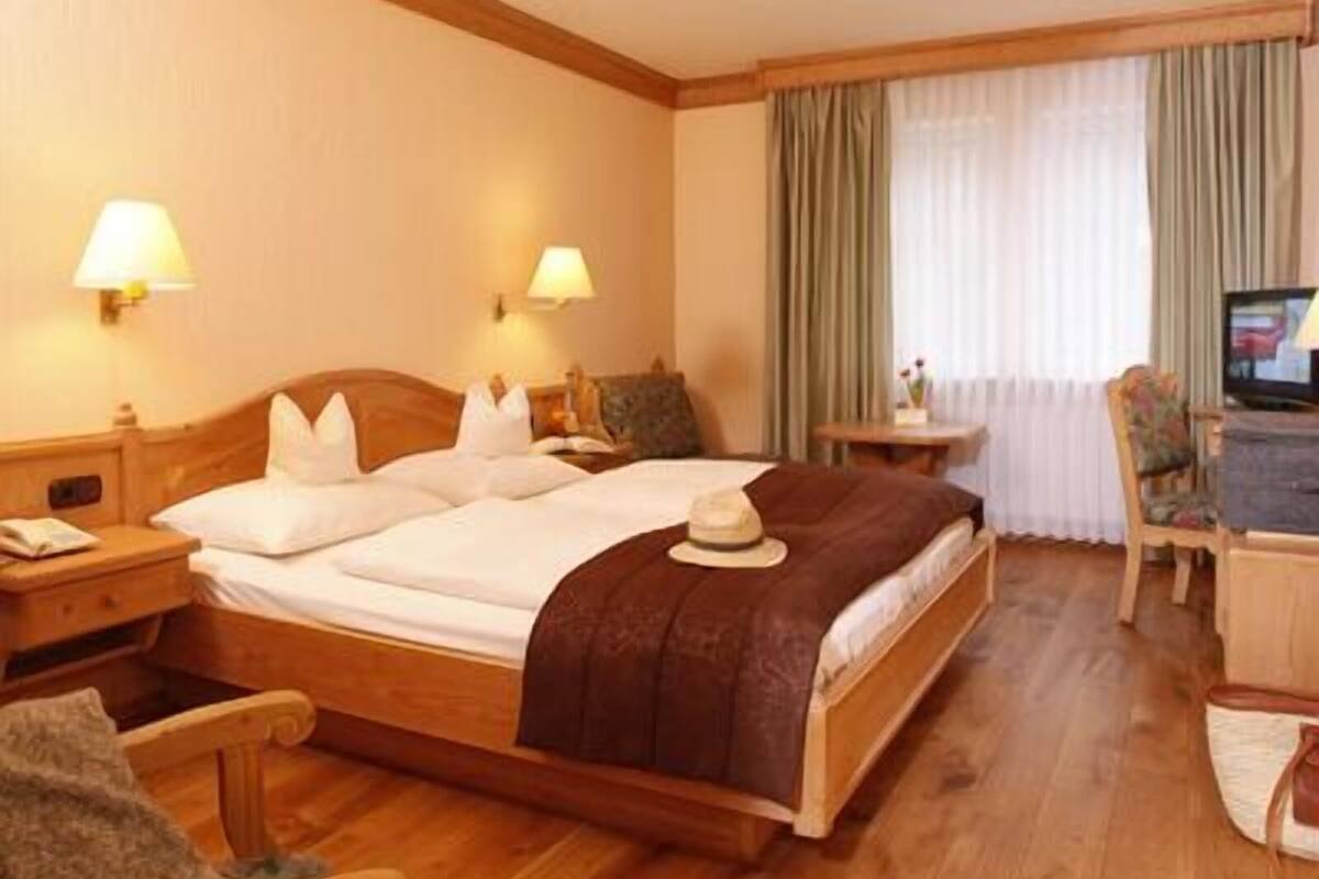 A hotel room with a wooden bed, two bedside lamps, a television, a desk, and a chair.