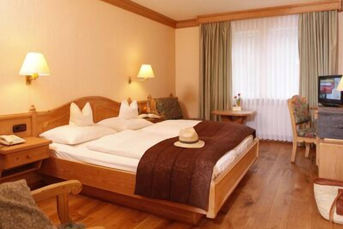 A hotel room with a wooden bed, two bedside tables with lamps, a television, a small desk, and a chair.