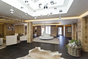 Um hall amplo com área de estar central, detalhes em madeira e teto com luminárias esféricas penduradas.
