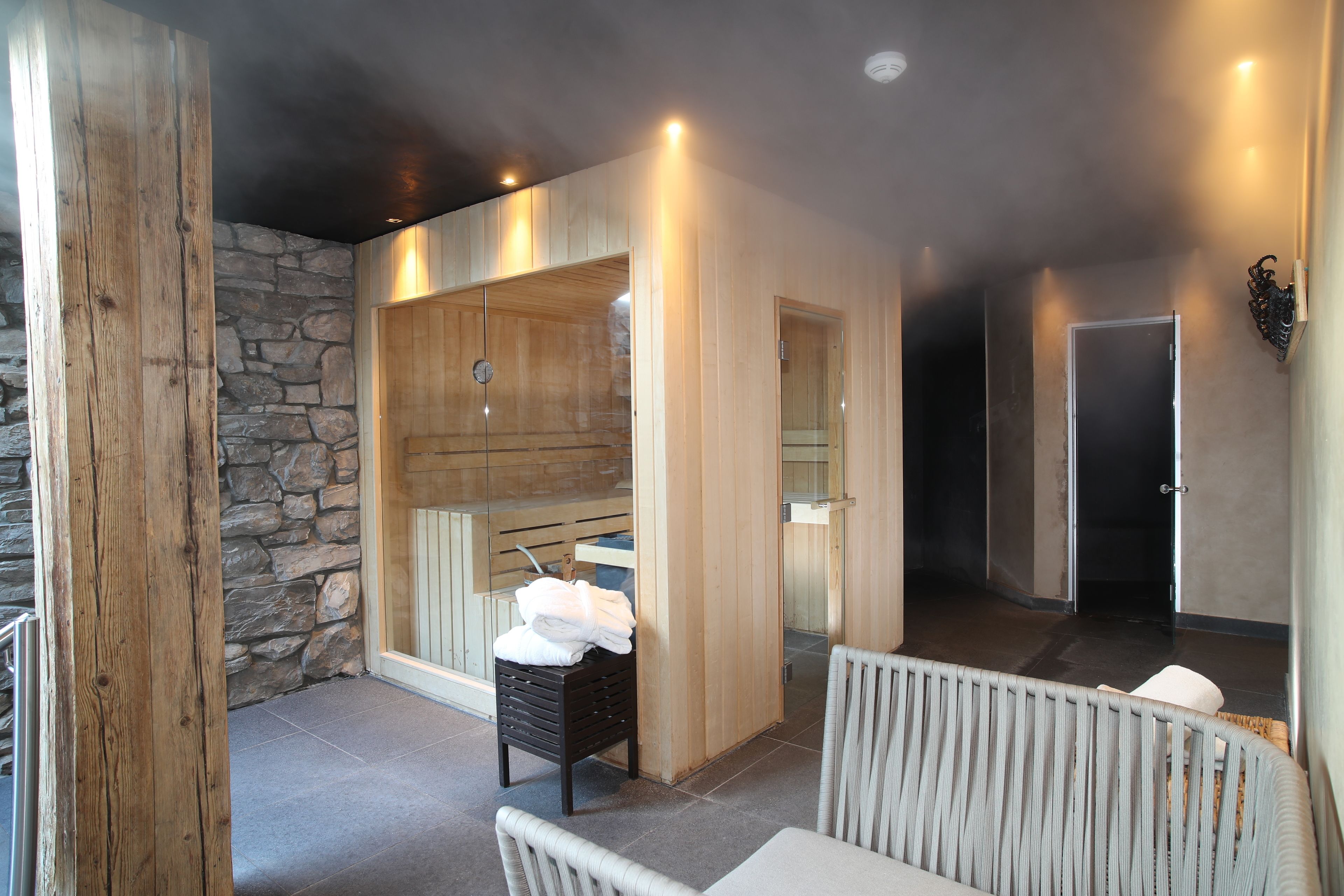 Un espacio de spa con pared de piedra, sauna de madera y asientos.