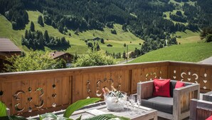A wooden deck with outdoor furniture, a table with glasses, and a view of green mountains and a clear sky. - Hotel de Rougemont & Spa (Rougemont)