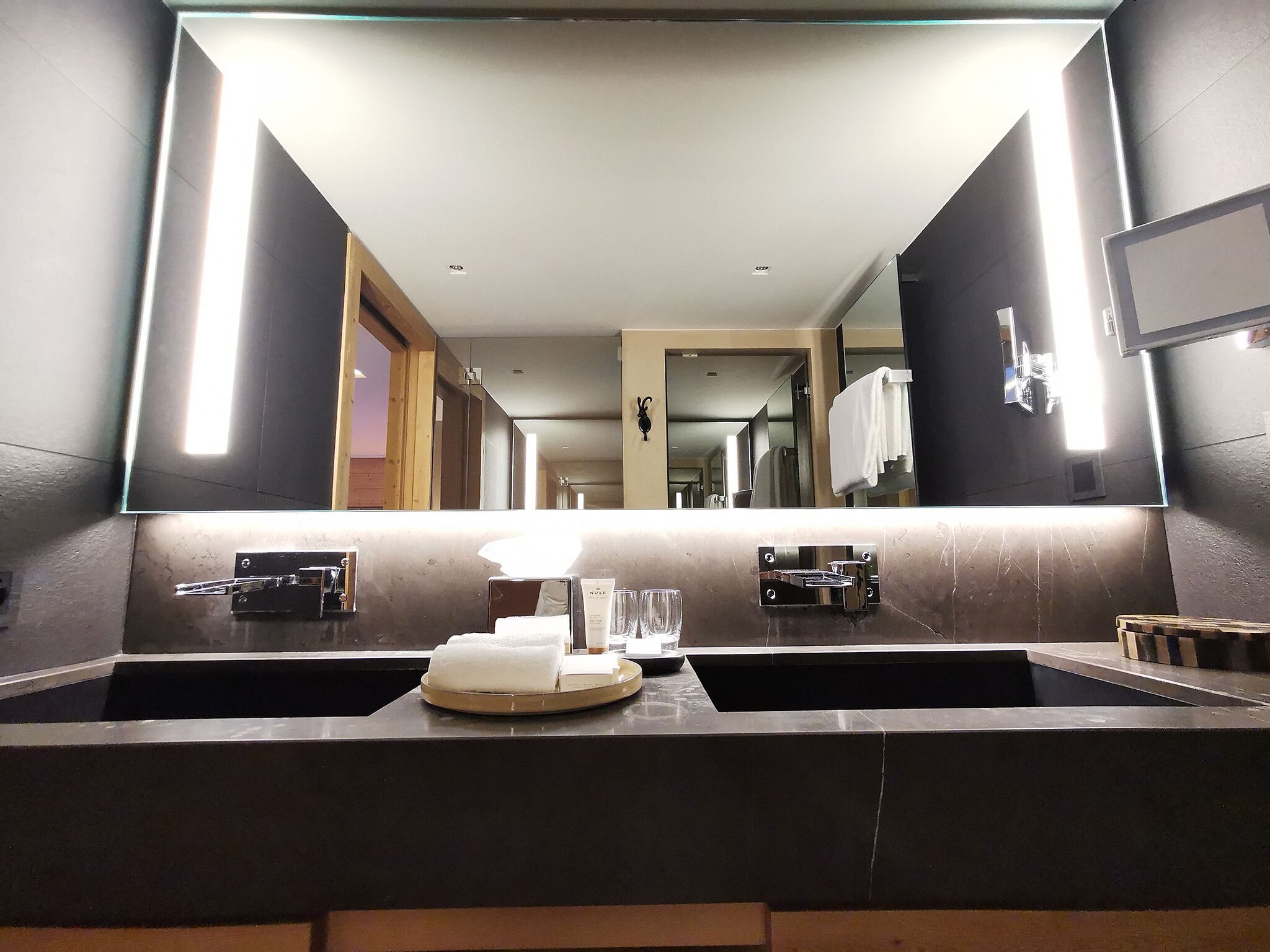 A modern bathroom with two sinks, a large mirror, and a towel rack.