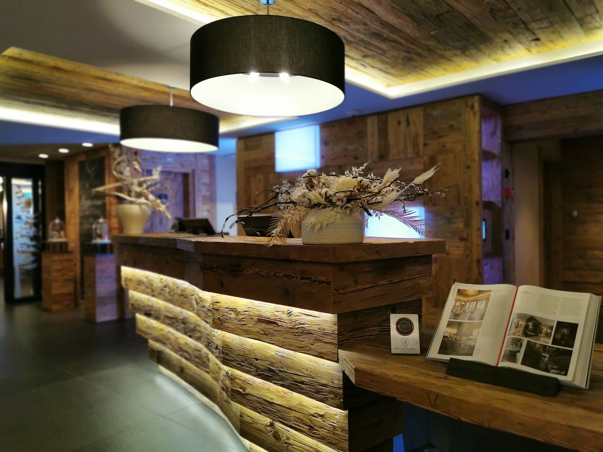 A wooden reception desk with a vase of dried flowers, a framed photo, and a plaque.