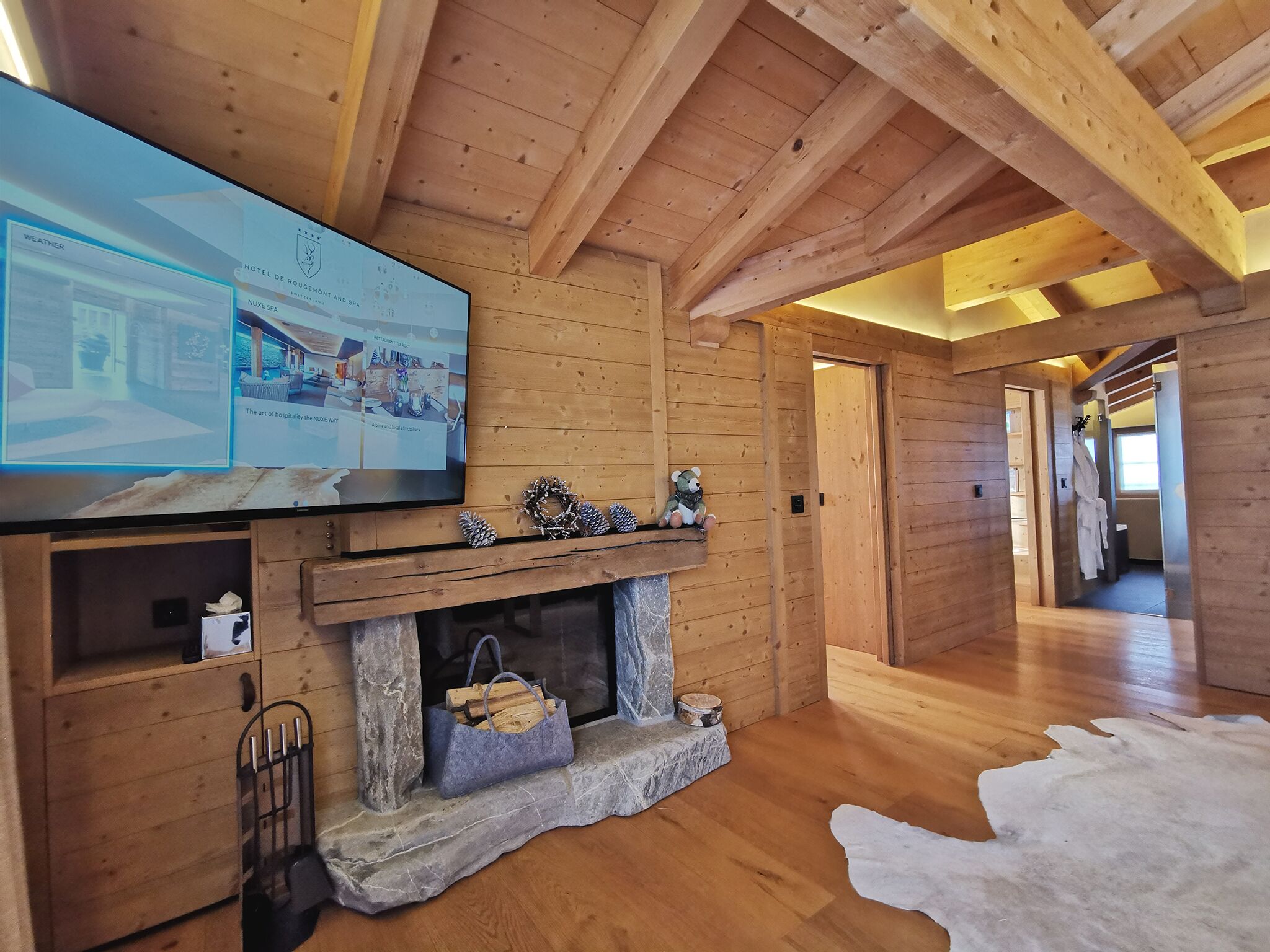 A wooden interior with a fireplace, a television displaying hotel information, and a hallway leading to another room.