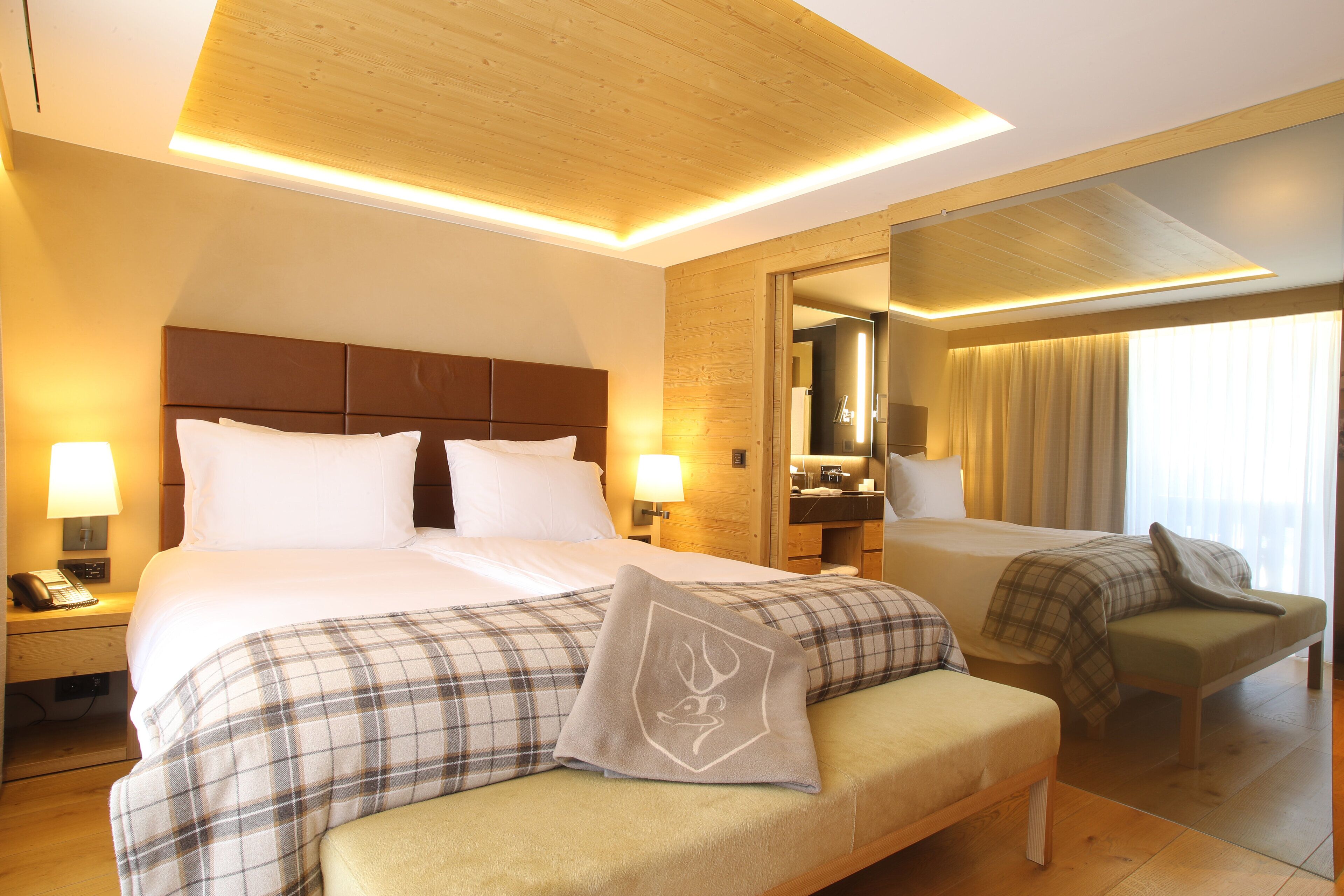 A hotel room with a large bed, a bedside table with a lamp, a chair, and a mirror.