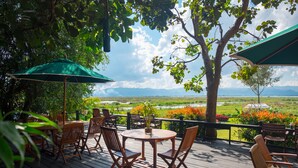 A wooden deck with outdoor seating, a green umbrella, and a view of a landscape with mountains and a river. - Amata Garden Resort (Nyaungshwe)