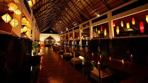 A dimly lit corridor with a high ceiling and hanging lanterns, leading to a central area with a traditional structure. - Amata Garden Resort (Nyaungshwe)