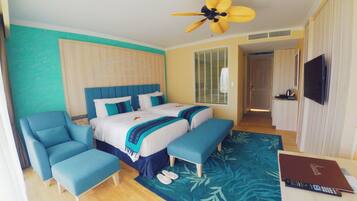 A hotel room with a bed, two armchairs, a ceiling fan, a TV, and a desk with a laptop.
