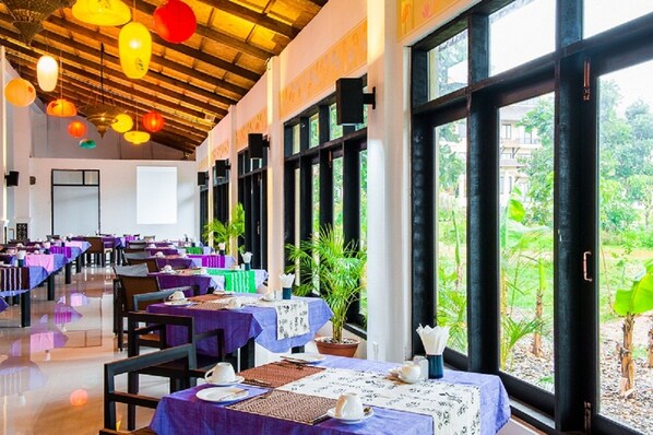 Un restaurante con varias mesas, techo de madera y amplios ventanales con vistas a zonas verdes.