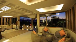 A modern interior with wicker furniture, a large window with a city view, and a ceiling with recessed lighting. - Amata Garden Resort (Nyaungshwe)