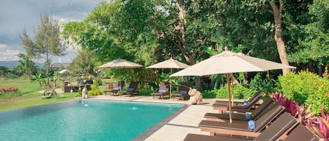 Una piscina al aire libre, sombrillas, sillones reclinables de piscina
