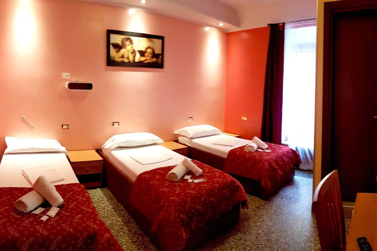 A hotel room with three single beds, a painting on the wall, and a television on the right.